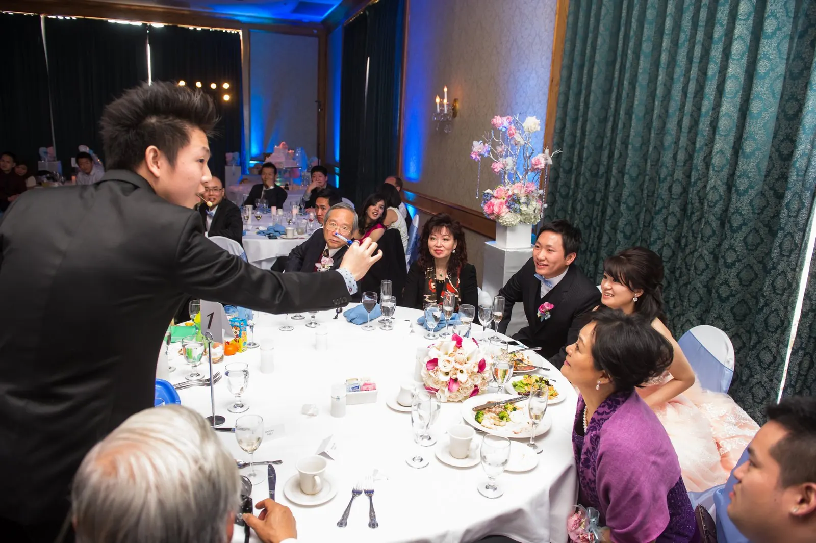 Johnny Wu performing card magic for a full table of guests in a ballroom